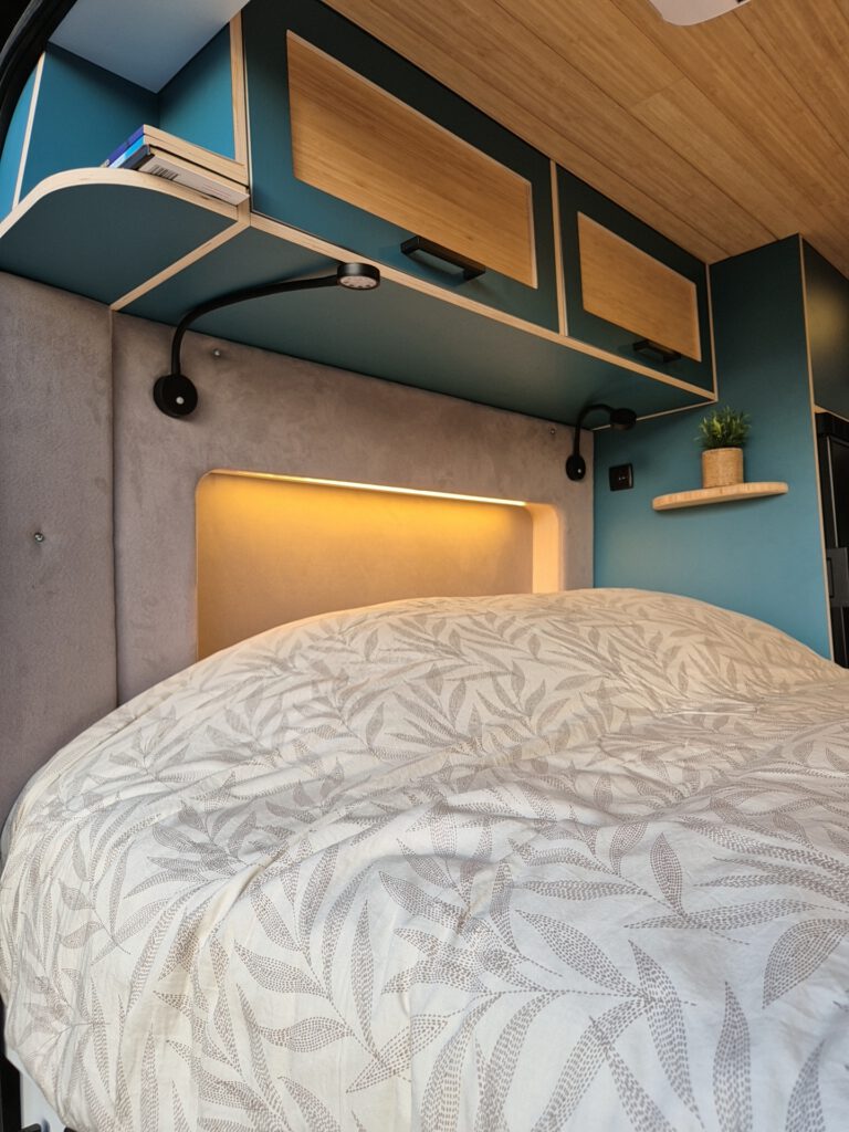 Bed in camper met blauwe inrichting en warme led verlichting