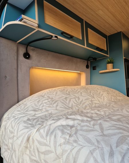 Bed in camper met blauwe inrichting en warme led verlichting